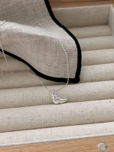 Macro detail of 925 silver croissant necklace on a textured cream jewelry display tray