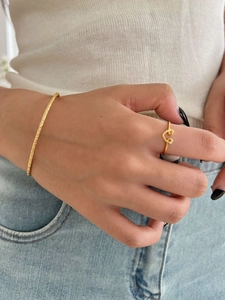 Detail shot of a matte gold textured bracelet and open heart ring worn by a model