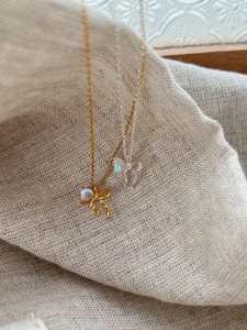 Close-up of gold and silver bow necklaces with heart-shaped moonstones on linen fabric