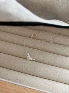 Macro detail of silver croissant pendant necklace showing fine metallic texture on fabric