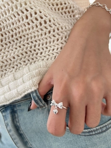 Detailed close-up of a S925 sterling silver bow ring with a dangling heart charm on hand