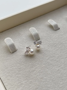 Detail of silver bow earrings with shiny stones and white pearls on a soft grey tray