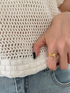 Detail shot of a golden bow ring with a heart charm worn against a knit sweater