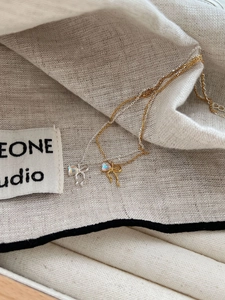 Macro detail of silver and gold bow pendants with iridescent moonstone on linen fabric
