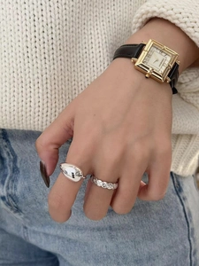 Close-up of a silver water drop ring and a quilted pattern ring on a model's hand