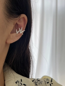 Detailed view of silver origami crane ear cuff worn on the ear without piercings