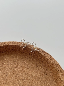 Détail de boucles d'oreilles ruban en argent 925 avec perle centrale sur support bois