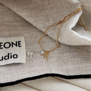Bowtie moonstone necklaces in gold and silver colors on elegant beige linen fabric