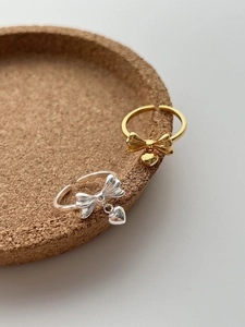 Detail of silver and gold bow rings with heart pendants on a cork tray display