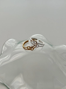 Detail of gold and silver S925 double-layer braided rings on a wavy glass tray