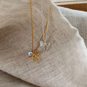 Elegant gold and silver moonstone bow necklaces on a beige linen background