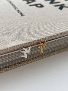 Brushed metal crane stud earrings in gold and silver finish placed on a book