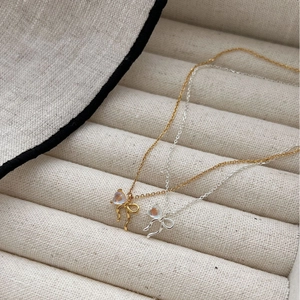 Elegant gold and silver moonstone bow pendant necklaces in a beige jewelry box