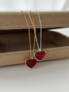 Detail of red enamel heart pendants on gold and silver chains draped over a jewelry box