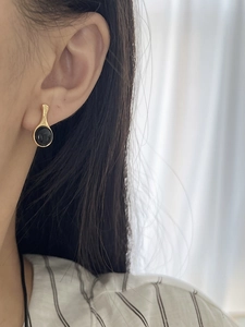 Close-up of a minimalist round black onyx earring on a model's ear with gold setting