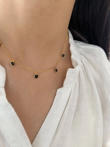 Gros plan d'un collier en chaîne dorée avec quatre pendentifs coeurs noirs sur un mannequin