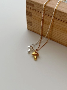 Detailed view of silver and gold mushroom pendants on minimalist chains over wood