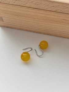 Detailed view of yellow agate bead earrings with silver hooks on a wooden box background