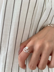 Close-up of 925 sterling silver pearl knot ring worn on a finger with striped background