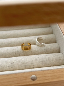 Makro-Detail von geschichteten Gold- und Silber-Ohrklemmen auf beigem Leinenetui