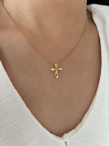 Close-up of minimalist gold cross necklace pendant on model neck with silver chain