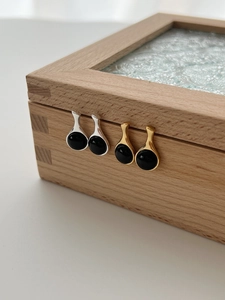 Detail view of gold and silver drop earrings set with black onyx on a wooden box