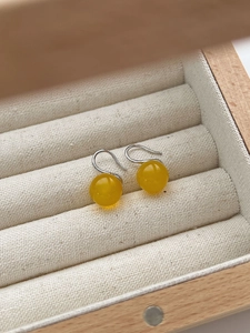 Macro detail of yellow agate bead earrings on soft fabric inside a wooden jewelry box
