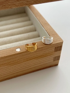 Detail von gold- und silbernen Ohrklemmen mit gerippter Struktur auf einer Holzbox