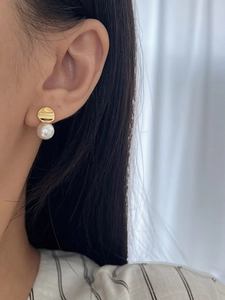 Close-up of golden hammered metal earring with a drop pearl on woman's ear