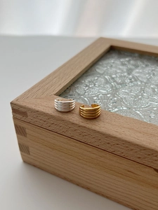 Detailansicht der gold- und silberfarbenen mehrschichtigen Ear Cuffs auf einer Holzbox
