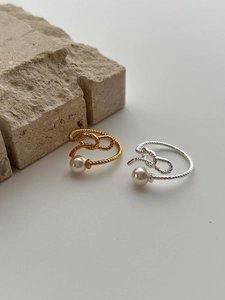 Detail of twisted silver and gold rings with white pearls on a stone backdrop