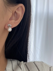 Close-up of minimalist silver pearl stud earring worn on ear with soft lighting