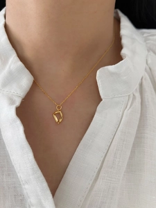 Close-up of a minimalist irregular gold pendant necklace worn on a white linen shirt