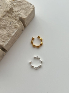 Detailansicht strukturierter Ohrklemmen in Gold und Silber auf minimalistischem Stein