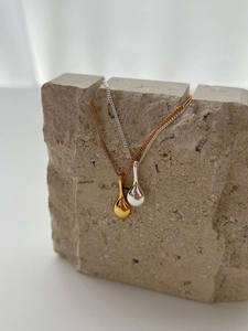 Détail de colliers avec pendentif bouteille de vin en or et argent sur présentoir en pierre