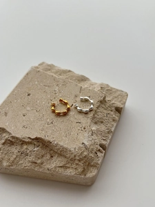 Detailansicht von silbernen und goldenen Ear Cuffs auf einem minimalistischen Steinsockel