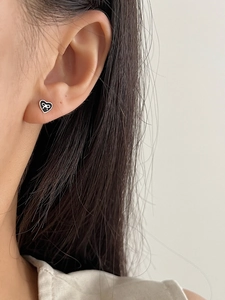 Close-up of heart-shaped silver earrings with black inlay and white bow detail