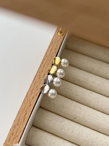 Close-up of four minimalist pearl stud earrings in gold and silver finish on a wooden box
