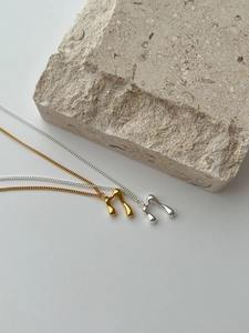 Detail of gold and silver irregular liquid metal music note necklaces on textured stone