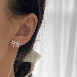 Sparkling silver bow knot stud earrings featuring micro-pave crystals on a model's ear