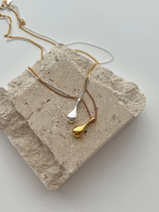 Détail de colliers avec pendentif goutte en or et argent sur support en pierre