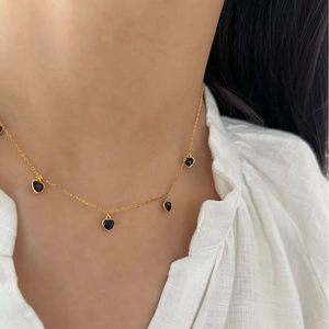 Élégant collier doré avec cinq petits pendentifs cœurs noirs porté sur chemise blanche