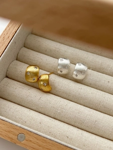 Dettaglio macro di orecchini in metallo spazzolato oro e argento con incisione
