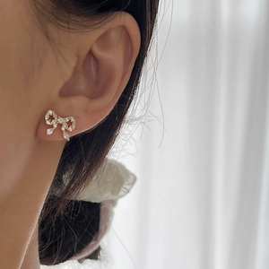 Sparkling crystal bow stud earrings with gold finish shown worn on earlobe for elegant look