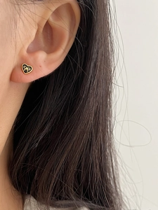 Macro detail of heart-shaped earring with black enamel and a golden bow on ear