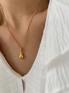 Gros plan d'un collier pendentif goutte doré minimaliste porté sur une chemise blanche
