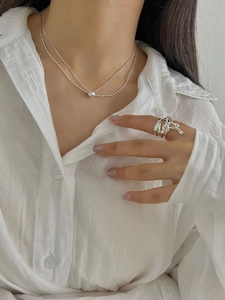 Detail of layered S925 silver necklace and geometric rings on a model with white shirt