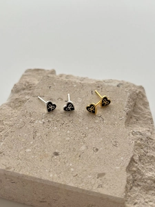 Detail of silver and gold heart stud earrings with black enamel bow on stone surface