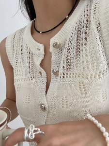 Detailed close-up of hollow knit texture and retro embossed metal buttons on the cream vest
