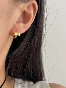 Close-up of a gold bow-shaped hoop earring worn on an earlobe with minimalist design
